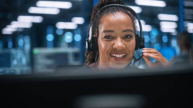 Çağrı Merkezi Ofisi: Dost canlısı Afrikalı Amerikalı Kadın Müşteri Desteği Uzmanı Kulaklıkla Konuşuyor, Bilgisayar kullanıyor. Müşteri Tecrübe Memuru Video Konferansı aracılığıyla Çevrimiçi Yardım Ediyor