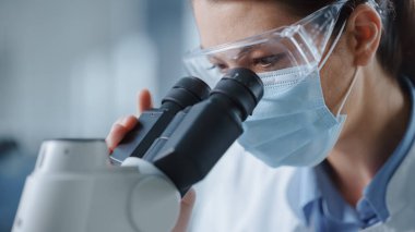 Mikroskop 'a bakan Maskeli ve Gözlüklü Kadın Bilimadamının Makro Yakın Çekimi. Modern Laboratuvarda Teknolojik Ekipmanlarla Molekül Örnekleri üzerinde çalışan Kadın Mikrobiyolog.