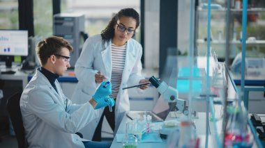 Modern Tıbbi Araştırma Laboratuvarı: Pipette, Dijital Tablet, Örnek Analiz Yapan, Konuşan İki Genç Bilim Adamının Portresi. Gelişmiş Laboratuvar 'da çok ırklı uzmanlardan oluşan çeşitli bir ekip çalışıyor.