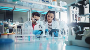Modern Tıbbi Araştırma Laboratuvarı: Mikroskop, Dijital Tablet, Örnek Analiz Yapan, Konuşan Latin ve Siyah Genç Bilim Adamlarının Portresi. Gelişmiş Laboratuvar 'da çeşitli uzmanlar çalışıyor.