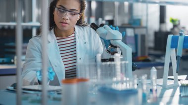 Tıbbi Bilimler Laboratuvarı: Mikroskop kullanarak Test Örnekleri Analizi Yapan Güzel Siyah Bilim Adamının Portresi. Hırslı Genç Biyoteknoloji Uzmanı, Gelişmiş Ekipmanlarla çalışıyor.