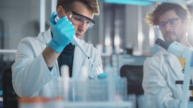 Modern Tıp Laboratuvarı: Genç Kafkas Erkek Araştırma Bilimadamı Test Tüpündeki Mikro Pipette kullanarak Kimyasal Sıvıları Karıştırıyor. Mikrobiyologlar biyoteknoloji araştırması yapıyor. Portre Çekimi
