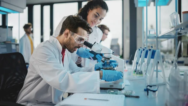 Modern Tıbbi Araştırma Laboratuvarı: Mikroskop, Dijital Tablet, Örnek Analiz Yapan, Konuşan Latin ve Siyah Genç Bilim Adamlarının Portresi. Gelişmiş Laboratuvar 'da çeşitli uzmanlar çalışıyor.