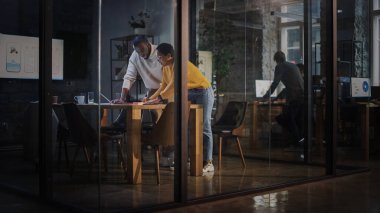 İki farklı etnik çeşitlilikte meslektaşın, bir ajanstaki cam duvarların arkasındaki toplantı odasında sohbet ediyorlar. Afrikalı Amerikalı Yaratıcı Direktör ve Kadın Proje Yöneticisi Laptop Bilgisayarında Çalışmayı Tartışıyor.