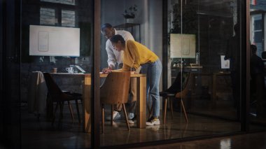 İki farklı etnik çeşitlilikte meslektaşın, bir ajanstaki cam duvarların arkasındaki toplantı odasında sohbet ediyorlar. Afrikalı Amerikalı Yaratıcı Direktör ve Kadın Proje Yöneticisi Laptop Bilgisayarında Çalışmayı Tartışıyor.