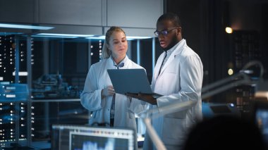 Modern Elektronik Araştırma, Geliştirme Tesisi: Yüksek Teknoloji Laboratuvarında Duran Mühendis ve Bilim adamı, Laptop Bilgisayarı Kullan, Konuş, Silikon Mikroçipler, Yarı iletkenler, Üretim Bilgisayarları