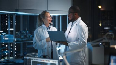 Modern Elektronik Araştırma, Geliştirme Tesisi: Yüksek Teknoloji Laboratuvarında Duran Mühendis ve Bilim adamı, Laptop Bilgisayarı Kullan, Konuş, Silikon Mikroçipler, Yarı iletkenler, Üretim Bilgisayarları