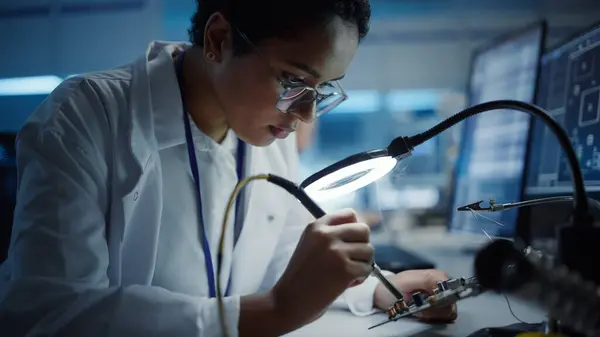 Modern Electronics Research, Development Facility: Black Female Engineer Does Computer Motherboard Soldering. Scientists Design PCB, Silicon Microchips, Semiconductors. Close-up Portrait Shot