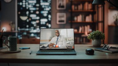 Konforlu Oturma Odasında Masada Duran Bir Erkek Doktora Video Çağrı ile Dizüstü bilgisayar. Arka planda Modern İç İşleri Stüdyosunda Büyük Şehir Penceresi ile Akşam.