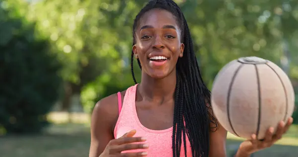 一个强壮的黑人年轻女子在户外看相机时抛掷篮筐球的肖像 微笑着面对陈规定型观念的女运动员 追随她的职业梦想 — 图库照片