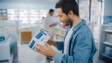 Eczanede: En İyi Yüz Maskesi Paketini Almaya Çalışan Yakışıklı Latin Erkeğin Portresi, Seçme Kutusu. Sağlık Ürünleriyle dolu raflar