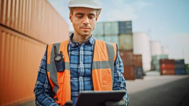 Beyaz Şapkalı Yakışıklı Kafkas Endüstriyel Mühendis, Turuncu Yüksek Görüş Yeleği, Kargo Konteynır Terminalinde Tablet Bilgisayar üzerinde çalışan Kareli Gömlek ve İş Eldiveni.