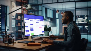 Yaratıcı Ev Oturma Odasında Masaüstü Bilgisayarı 'nda çalışan yakışıklı siyahi Amerikalı Uzman. Serbest Erkek, Yeni Müşteri ve İşveren ile Randevu Almak İçin Takvimini Kontrol Ediyor.