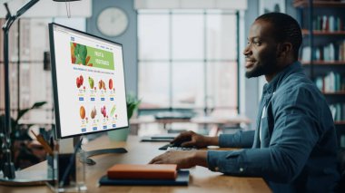 Yakışıklı Siyah Afro-Amerikalı, Akşam Yemeği İçin Taze Sebze Siparişi Vermek İçin Bakkaliye Web Sayfası ile Masaüstü Bilgisayarı Kullanıyor. Modern Dev Uygulama 'da yaşıyor..