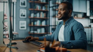 Yaratıcı Ev Oturma Odasında Masaüstü Bilgisayarı 'nda çalışan yakışıklı siyahi Amerikalı Uzman. Serbest Erkek Müşteriler ve İşverenler için Mali Sunum Raporu üzerinde çalışıyor.