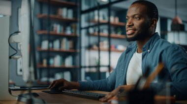 Yaratıcı Ev Oturma Odasında Masaüstü Bilgisayarı 'nda çalışan yakışıklı siyahi Amerikalı Uzman. Serbest Erkek Müşteriler ve İşverenler için Mali Sunum Raporu üzerinde çalışıyor.