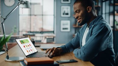 Yakışıklı Siyah Afro-Amerikalı, yemek yapmak için taze sebze siparişi vermek için Diz üstü bilgisayarı ve market teslimatı web sayfasını kullanıyor. Modern Dev Uygulama 'da yaşıyor..