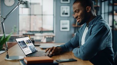 Yaratıcı Ev Oturma Odasında dizüstü bilgisayar üzerinde çalışan yakışıklı siyahi Amerikalı Uzman. Serbest Erkek Finansal Piyasa Analizi için Haberler Okumakta ve Müşteri ve İşveren Raporu.