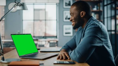 Yakışıklı siyahi Amerikalı Uzman, Ev Oturma Odası 'nda Yeşil Ekran Moklonu ile Laptop' ta Video Çağrısında Sohbet ediyor. Sosyal ağlarda Müşterilerle İnternet üzerinden Konuşan Serbest Adam.