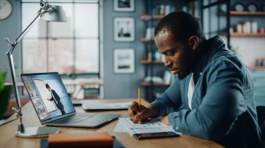 Oturma odasında masanın arkasında otururken bilgisayarında Afrikalı Amerikalı adamın online video dersi var. Serbest Çalışan Yetenekleri Üzerinde Çalışan Ya da İnternet Üzerinde Ödev Yapan Öğrenci.