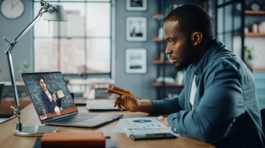 Oturma odasında masanın arkasında otururken bilgisayarında Afrikalı Amerikalı adamın online video dersi var. Serbest Çalışan Yetenekleri Üzerinde Çalışan Ya da İnternet Üzerinde Ödev Yapan Öğrenci.
