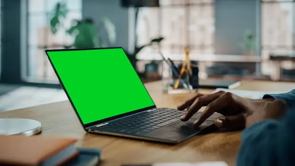 Close Up on Hands of Black African American Specialist Working on Laptop Computer with Green Screen Mock Up Display at Home Living Room. Freelance Man Chatting to Clients Over the Internet.