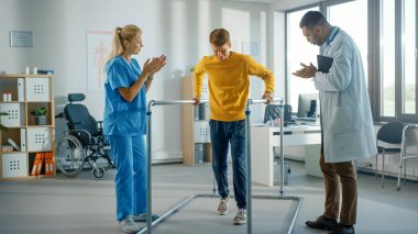 Hastane Fizik Terapisi: Yaralı Genç Erkek Hasta portresi Başarılı bir şekilde Paralel Paralel Barlarda Yürüyor. Fizyoterapist, Rehabilitasyon Doktoru, Yardım, Yardım, Engelli Kişi