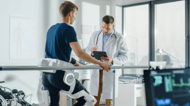 Modern Hastane Fizik Terapisi: Doktor Tablet Bilgisayar Kullanıyor, Koşu bandında Yürüyen Engelli Hastanın Gelişmiş Robotik Dış iskelet Bacakları Giymesine Yardım Ediyor. Fizyoterapi rehabilitasyon teknolojisi.