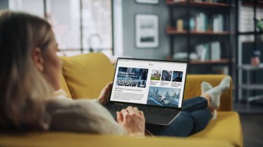 Güzel Beyaz Kadın, Kanepe üzerinde yatarken Ev Oturma Odasında Son Haberleri Okumak İçin Dizüstü bilgisayar kullanıyor. Evden Çalışan Serbest Uzman İnternet Sörfü.