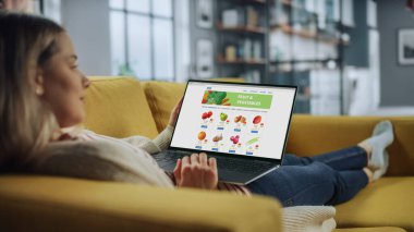 Güzel Beyaz Dişi, Taze Meyve ve Sebze Siparişi Vermek İçin Laptop Bilgisayar Kullanıyor. Ev Oturma Odası 'nda. Evden Çalışan Serbest Uzman İnternet Sörfü.