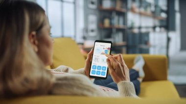 Güzel Otantik Kadın Bir Kanepede uzanırken Evde Oturma Odası 'nda Yemek Teslimatı Uygulaması ile Akıllı Telefon Kullanıyor. Katalog ve Seçme 'ye bakıyor. Akşam yemeği için ne sipariş etmeli?.