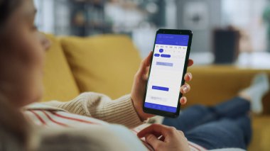 Güzel Otantik Kadın Kanepe üzerinde yatarken Evde Oturma Odasında Takvim Uygulaması ile Akıllı Telefon Kullanıyor. Planlar yapıyor ve bir günlük etkinlik programını kontrol ediyor..