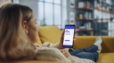 Güzel Otantik Kadın Kanepe üzerinde yatarken Evde Oturma Odasında Takvim Uygulaması ile Akıllı Telefon Kullanıyor. Planlar yapıyor ve bir günlük etkinlik programını kontrol ediyor..