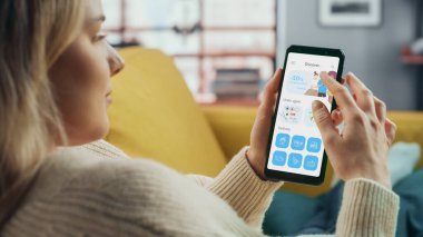 Güzel Otantik Kadın Bir Kanepede uzanırken Evde Oturma Odası 'nda Yemek Teslimatı Uygulaması ile Akıllı Telefon Kullanıyor. Katalog ve Seçme 'ye bakıyor. Akşam yemeği için ne sipariş etmeli?.