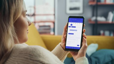 Güzel Otantik Kadın Kanepe üzerinde yatarken Evde Oturma Odasında Takvim Uygulaması ile Akıllı Telefon Kullanıyor. Planlar yapıyor ve bir günlük etkinlik programını kontrol ediyor..