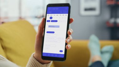 Güzel Otantik Kadın Kanepe üzerinde yatarken Evde Oturma Odasında Takvim Uygulaması ile Akıllı Telefon Kullanıyor. Planlar yapıyor ve bir günlük etkinlik programını kontrol ediyor..