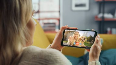 Ev Oturma Odası 'ndan Smartphone' da Güzel Arkadaşı ile Bir Köpekle Oynayan Bir Kadın Sohbetinin Kapanışı. Serbest Çalışan İnternetten Bir Müşteriyle Sohbet Ediyor.