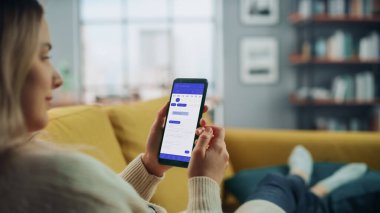 Güzel Otantik Kadın Kanepe üzerinde yatarken Evde Oturma Odasında Takvim Uygulaması ile Akıllı Telefon Kullanıyor. Planlar yapıyor ve bir günlük etkinlik programını kontrol ediyor..