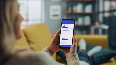 Güzel Otantik Kadın Kanepe üzerinde yatarken Evde Oturma Odasında Takvim Uygulaması ile Akıllı Telefon Kullanıyor. Planlar yapıyor ve bir günlük etkinlik programını kontrol ediyor..