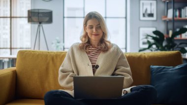 Kafkasyalı güzel bir uzman rahat bir koltukta otururken şık bir evde oturma odasında dizüstü bilgisayarla çalışıyor. Serbest Kadın İnternet Taraması, Sosyal Ağ Kullanımı, Daire Eğlencesi.