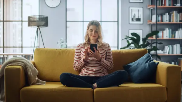 漂亮的白人女性坐在舒适的沙发沙发上 在时尚的客厅里用智能手机 年轻女子在家休息 浏览互联网 利用社交网络 享受平淡的生活 — 图库照片