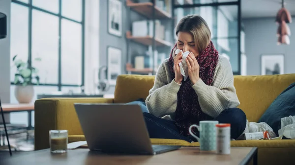 Ill Young Female Blowing Her Nose and Calling into Office with Video Phone Call from Cozy Living Room. Sick and Nauseous Woman in Warm Scarf is Using Laptop, Watching Movies.