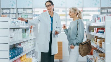 Eczane: Profesyonel Eczacı Güzel Yaşlı Kadın Müşteriye Tıbbi Tavsiye, Tavsiye ve Konuşmayla Yardım Ediyor. İlaç, hap, sağlık hizmeti ve güzellik ürünleriyle dolu bir eczane.