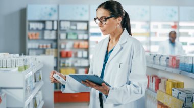 Eczane: Kafkasyalı güzel eczacı dijital tablet bilgisayar kullanıyor, ilaç, vitamin ve sağlık ürünlerini kontrol ediyor. Eczacı dükkanında profesyonel eczacı.