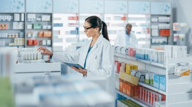 Eczane: Kafkasyalı güzel eczacı dijital tablet bilgisayar kullanıyor, ilaç, vitamin ve sağlık ürünlerini kontrol ediyor. Eczacı dükkanında profesyonel eczacı.