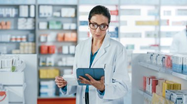 Eczane: Kafkasyalı güzel eczacı dijital tablet bilgisayar kullanıyor, ilaç, vitamin ve sağlık ürünlerini kontrol ediyor. Eczacı dükkanında profesyonel eczacı.