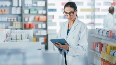 Eczane: Kafkasyalı güzel eczacı dijital tablet bilgisayar kullanıyor, ilaç, vitamin ve sağlık ürünlerini kontrol ediyor. Eczacı dükkanında profesyonel eczacı.