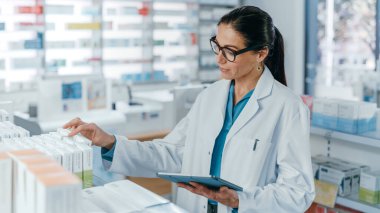 Eczane: Kafkasyalı güzel eczacı dijital tablet bilgisayar kullanıyor, ilaç, vitamin ve sağlık ürünlerini kontrol ediyor. Eczacı dükkanında profesyonel eczacı.