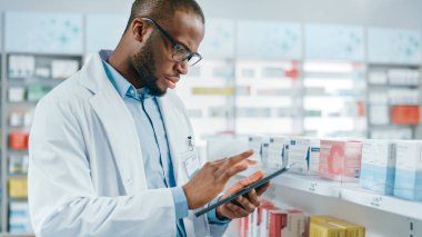 Eczane: Profesyonel Siyah Eczacının Portresi Dijital Tablet Bilgisayar kullanıyor, İlaç, İlaç, Raftaki Vitaminler Envanterini Kontrol Ediyor. Eczanedeki Eczacı Sağlık Ürünleri Düzenleme