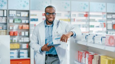 Eczane: Profesyonel Kendine Güvenen Siyah Eczacının Portresi Dijital Tablet Bilgisayar kullanıyor, Tıp Envanterini Kontrol ediyor, Kameraya Bakıyor ve Gülümsüyor. Sağlık Ürünleri olan eczane